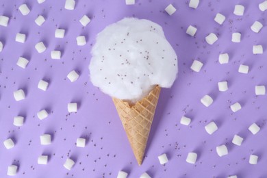 Photo of Sweet cotton candy in waffle cone surrounded by marshmallows on purple background, flat lay