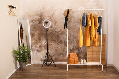 Photo of Stylish clothes on rack, mirror and ring light in room