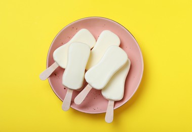 Photo of Plate with glazed ice cream bars on yellow background, top view