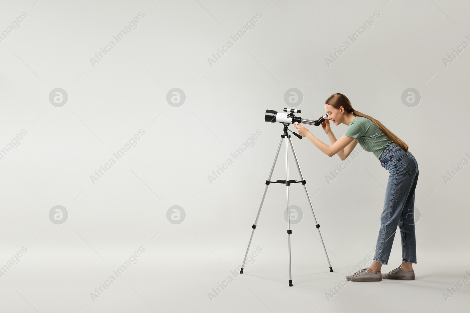 Photo of Young astronomer looking at stars through telescope on grey background, space for text