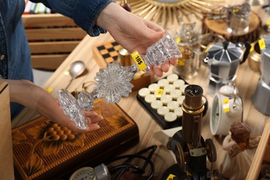 Photo of Woman holding beautiful glass candlestick near table with different stuff, closeup. Garage sale