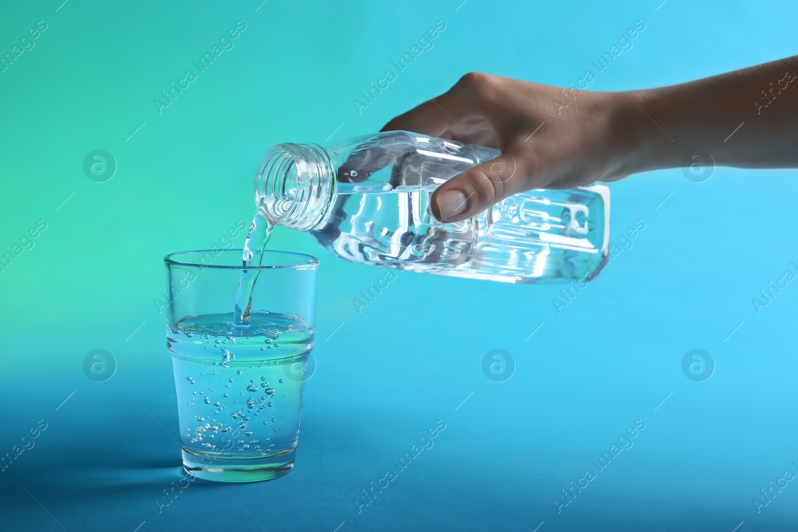 Photo of Woman pouring water from bottle into glass on blue background, closeup