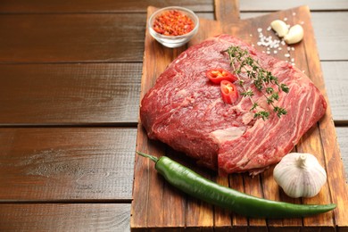 Photo of Fresh raw beef cut with spices on wooden table. Space for text