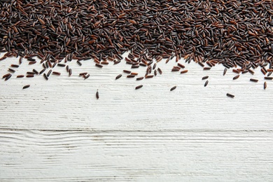 Photo of Uncooked black rice on white wooden background. Space for text