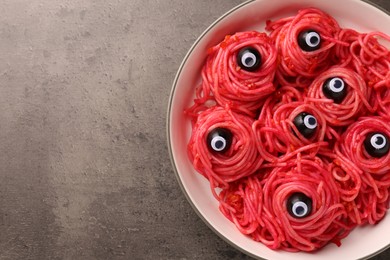 Red pasta with decorative eyes and olives in bowl on grey textured table, top view with space for text. Halloween food