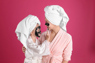 Photo of Happy mother and daughter with black facial masks on pink background