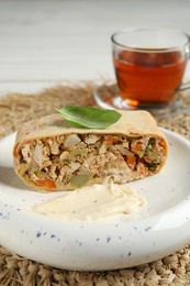 Photo of Piece of strudel with chicken, vegetables, sauce and tea on wicker mat, closeup