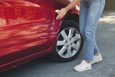 Photo of Young woman near car with scratch outdoors, closeup