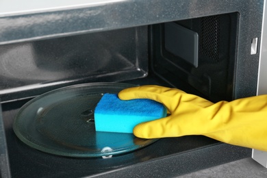 Woman cleaning microwave oven with sponge, closeup