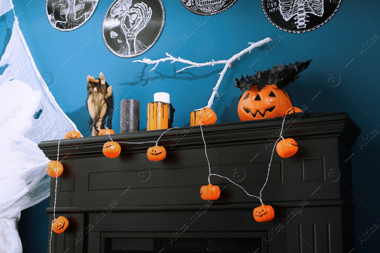 Photo of Jack-o'-lantern lights and different Halloween decorations on black fireplace near blue wall