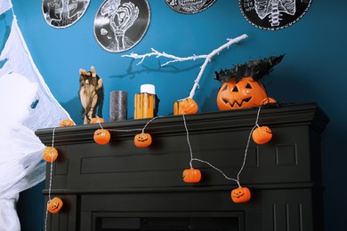 Jack-o'-lantern lights and different Halloween decorations on black fireplace near blue wall