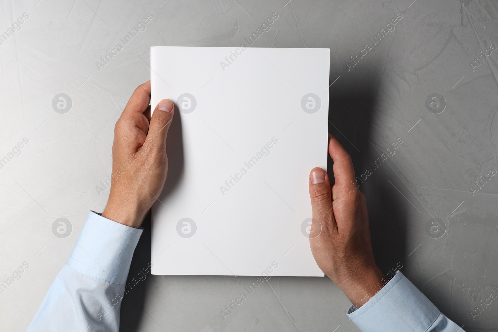 Photo of Man holding blank notebook at light grey table, top view. Mockup for design