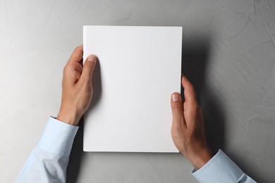 Man holding blank notebook at light grey table, top view. Mockup for design