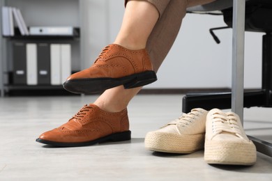 Photo of Comfortable sneakers near businesswoman in elegant shoes indoors, closeup