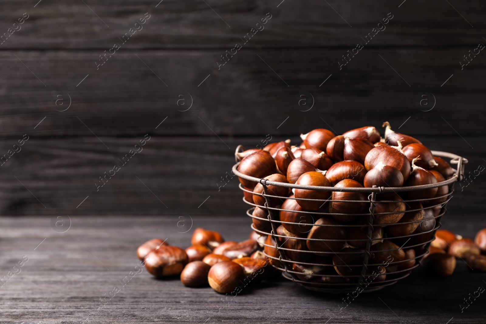 Photo of Fresh sweet edible chestnuts in basket on black wooden table. Space for text