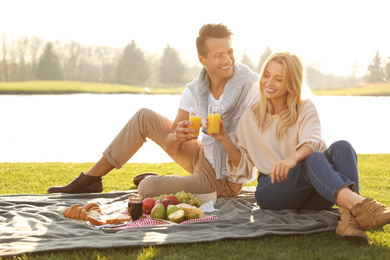 Happy young couple having picnic near lake on sunny day