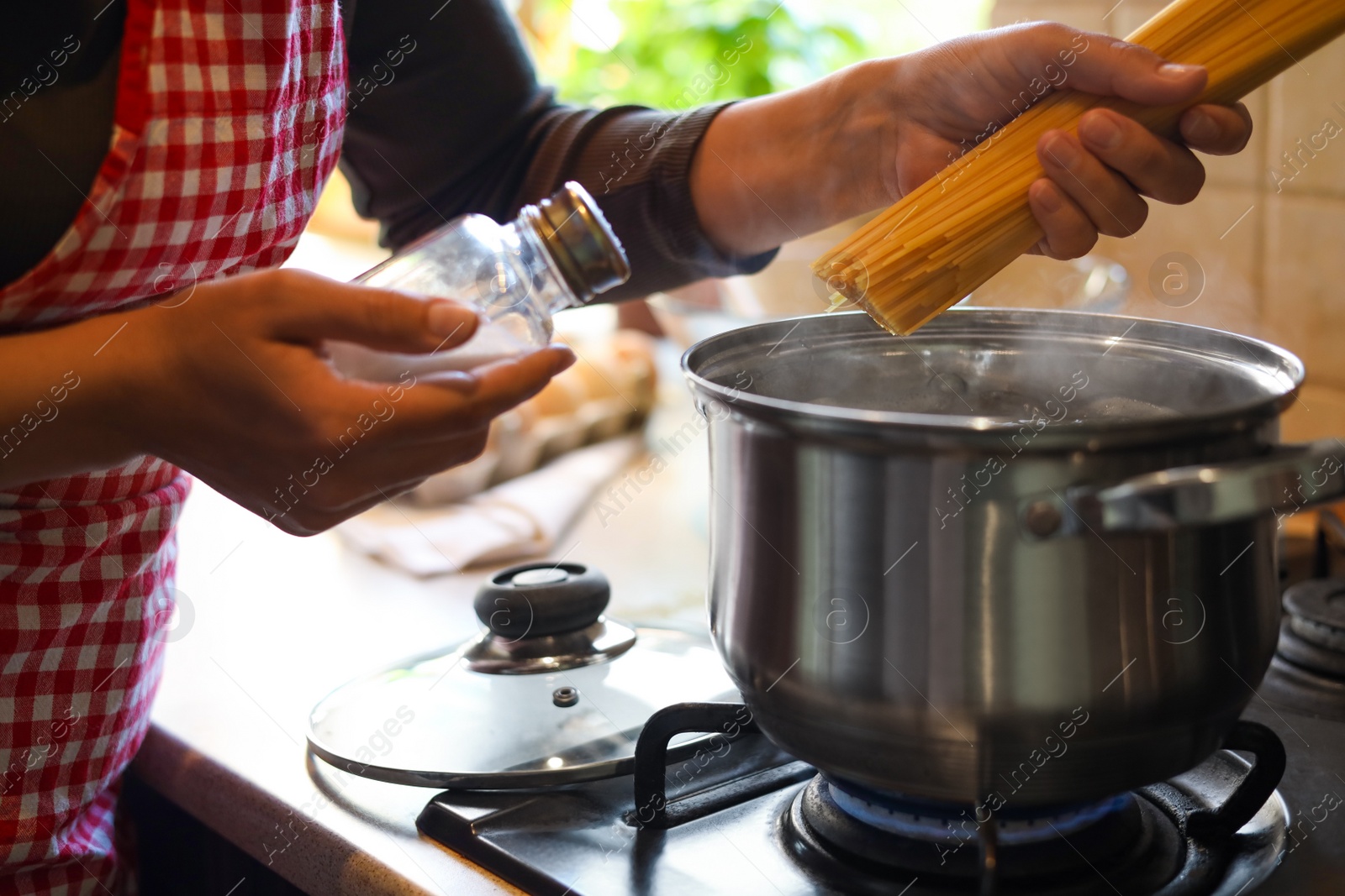 Photo of Woman cooking spaghetti on stove in kitchen, closeup