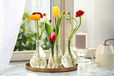 Photo of Different beautiful spring flowers in glassware, watering can and candle on window sill