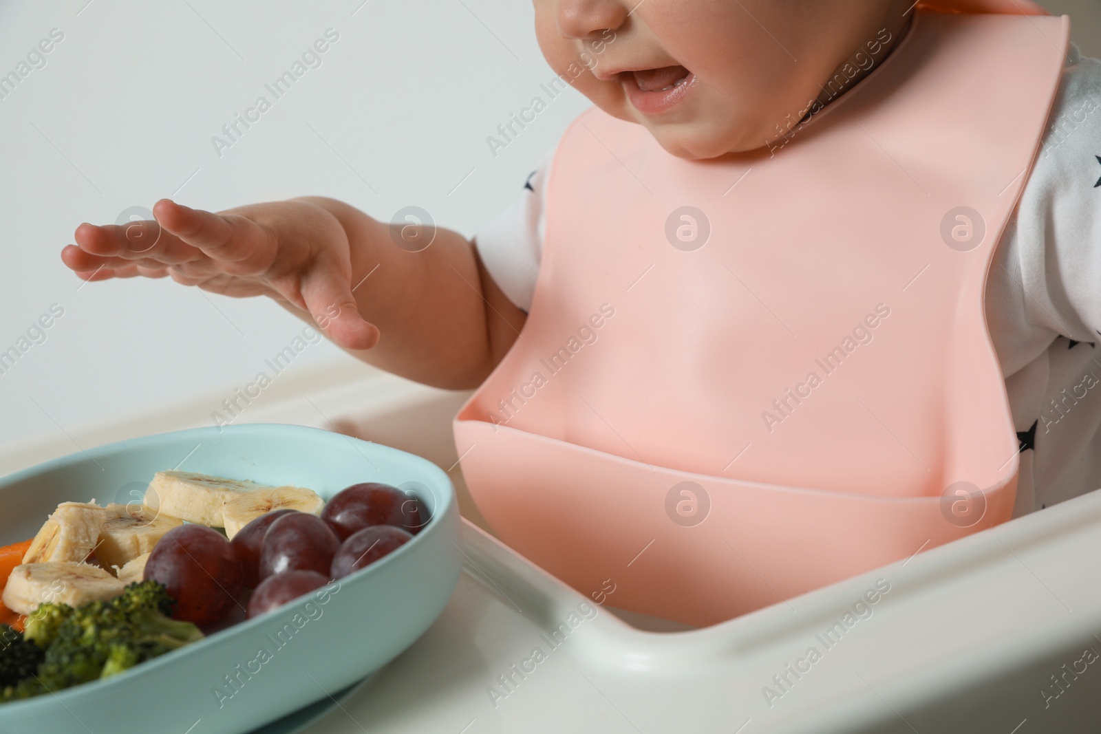 Photo of Cute little baby wearing bib while eating on white background, closeup