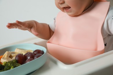 Photo of Cute little baby wearing bib while eating on white background, closeup