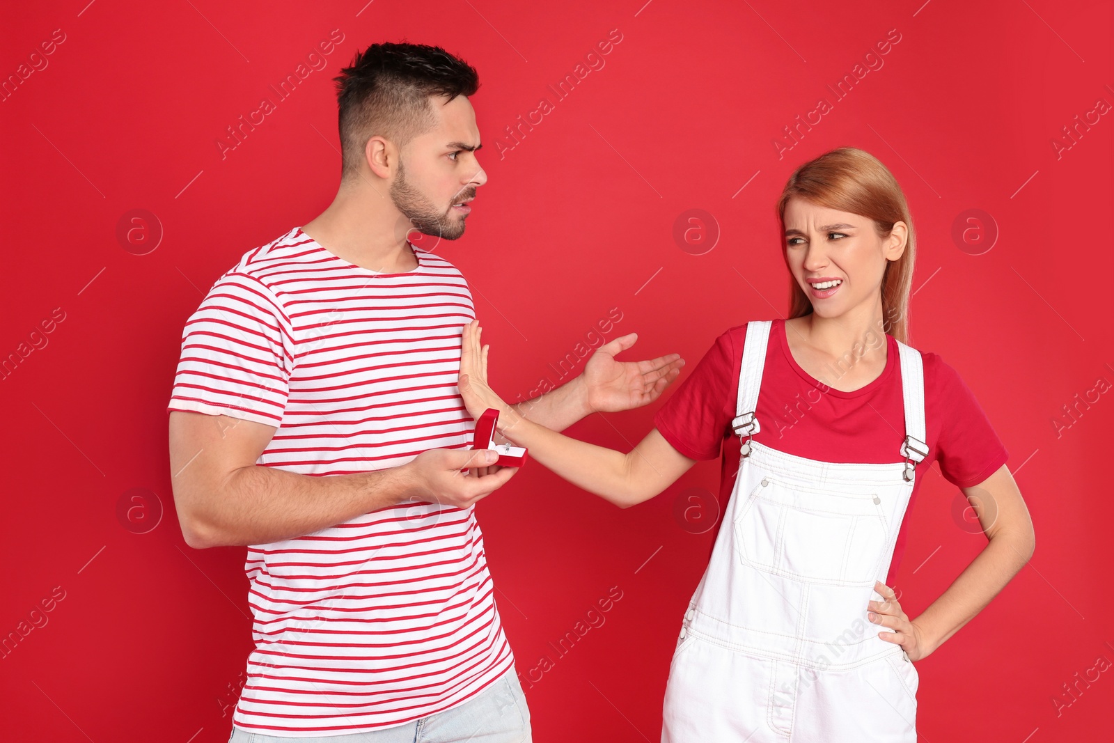 Photo of Young woman rejecting engagement ring from boyfriend on red background