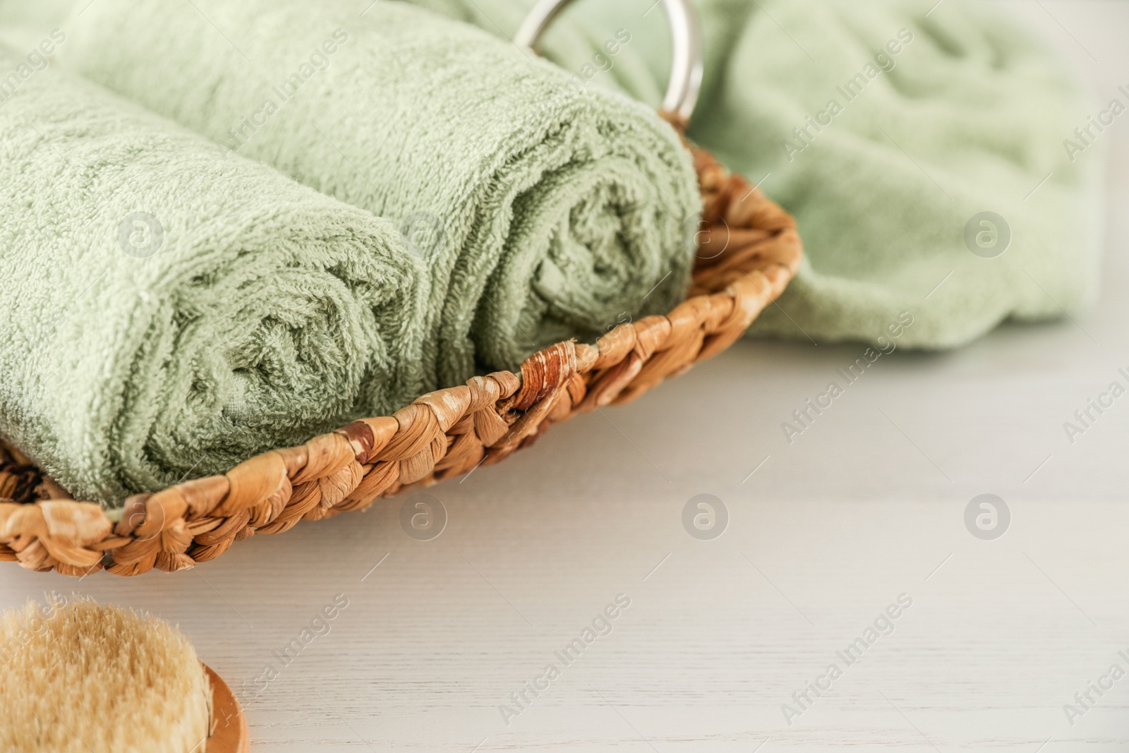 Photo of Wicker basket with rolled towels on white wooden table, closeup
