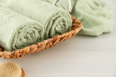 Wicker basket with rolled towels on white wooden table, closeup