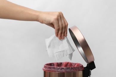 Photo of Woman putting paper tissue into trash bin on light background, closeup