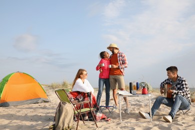 Friends resting near camping tent on sandy beach