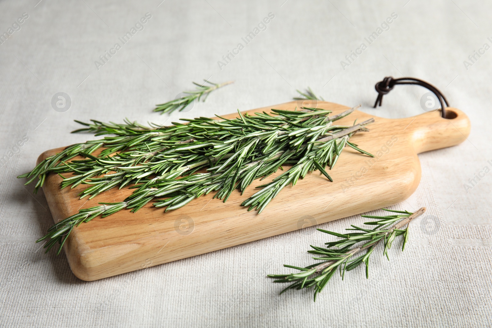 Photo of Wooden board with fresh rosemary twigs on fabric