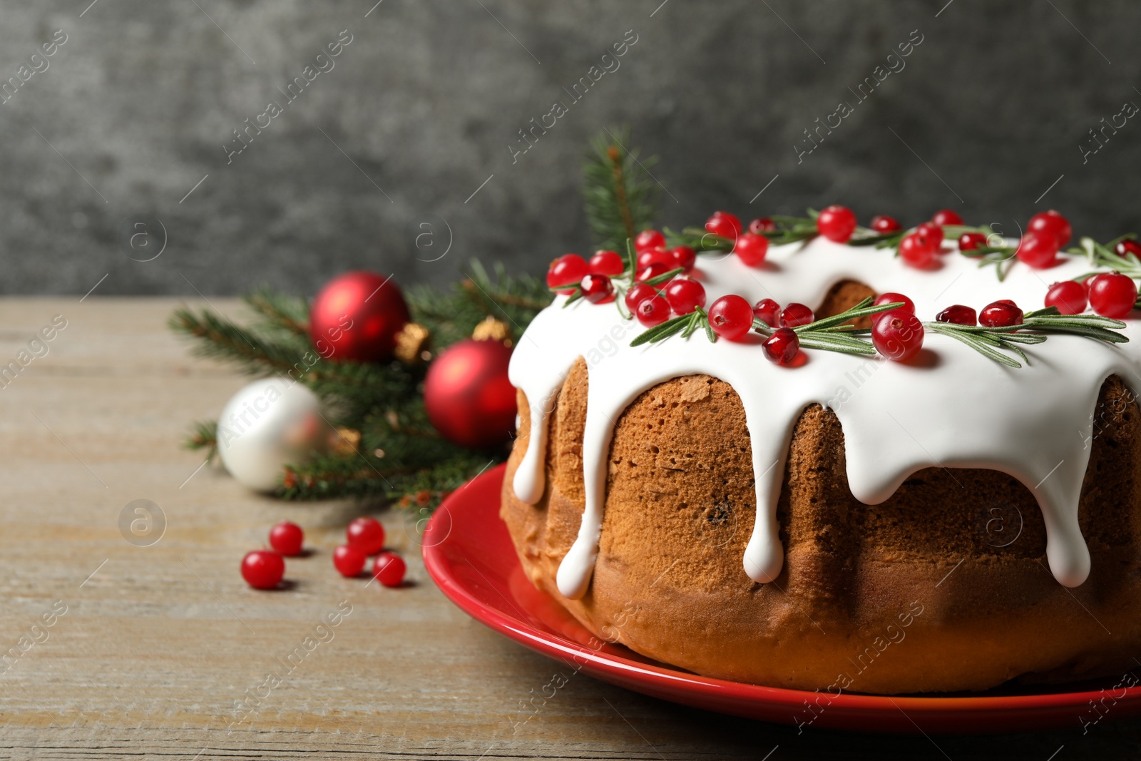 Photo of Traditional Christmas cake decorated with glaze, pomegranate seeds, cranberries and rosemary on wooden table, space for text