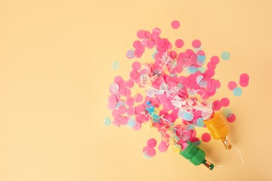 Photo of Colorful confetti and serpentine bursting out of party poppers on beige background, flat lay. Space for text