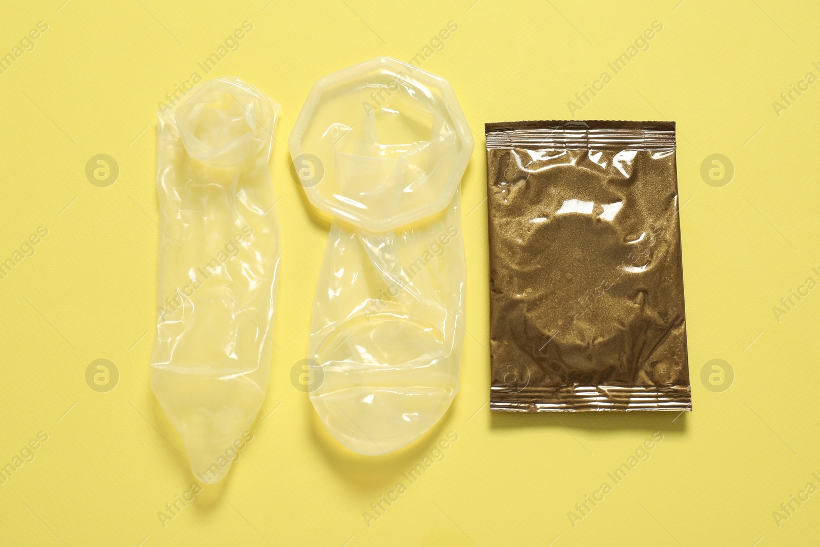 Photo of Unrolled female, male condoms and package on yellow background, flat lay. Safe sex