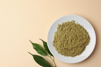 Photo of Henna powder and green leaves on beige background, flat lay with space for text. Natural hair coloring