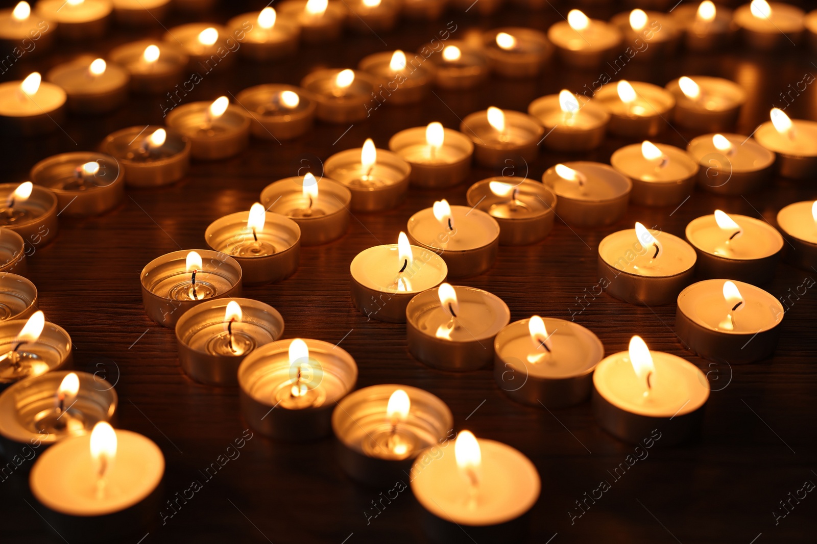 Photo of Burning candles on wooden table in darkness