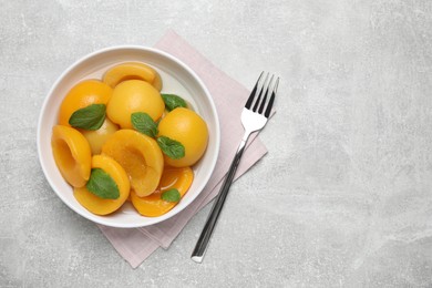 Photo of Canned peach halves and fork on light table, flat lay. Space or text