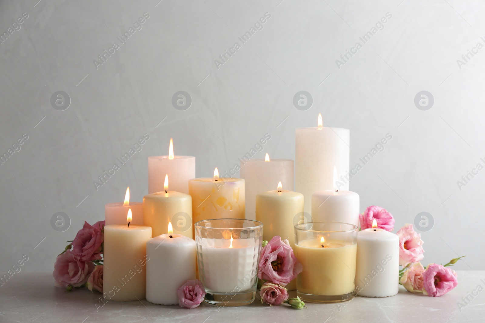 Photo of Composition with burning candles on table against light background