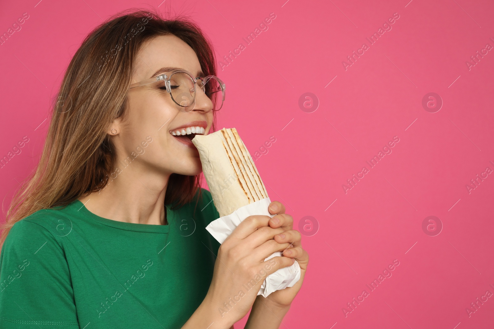 Photo of Young woman eating delicious shawarma on pink background, space for text