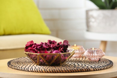 Photo of Aromatic potpourri of dried flowers in bowl and burning candles on wooden table indoors