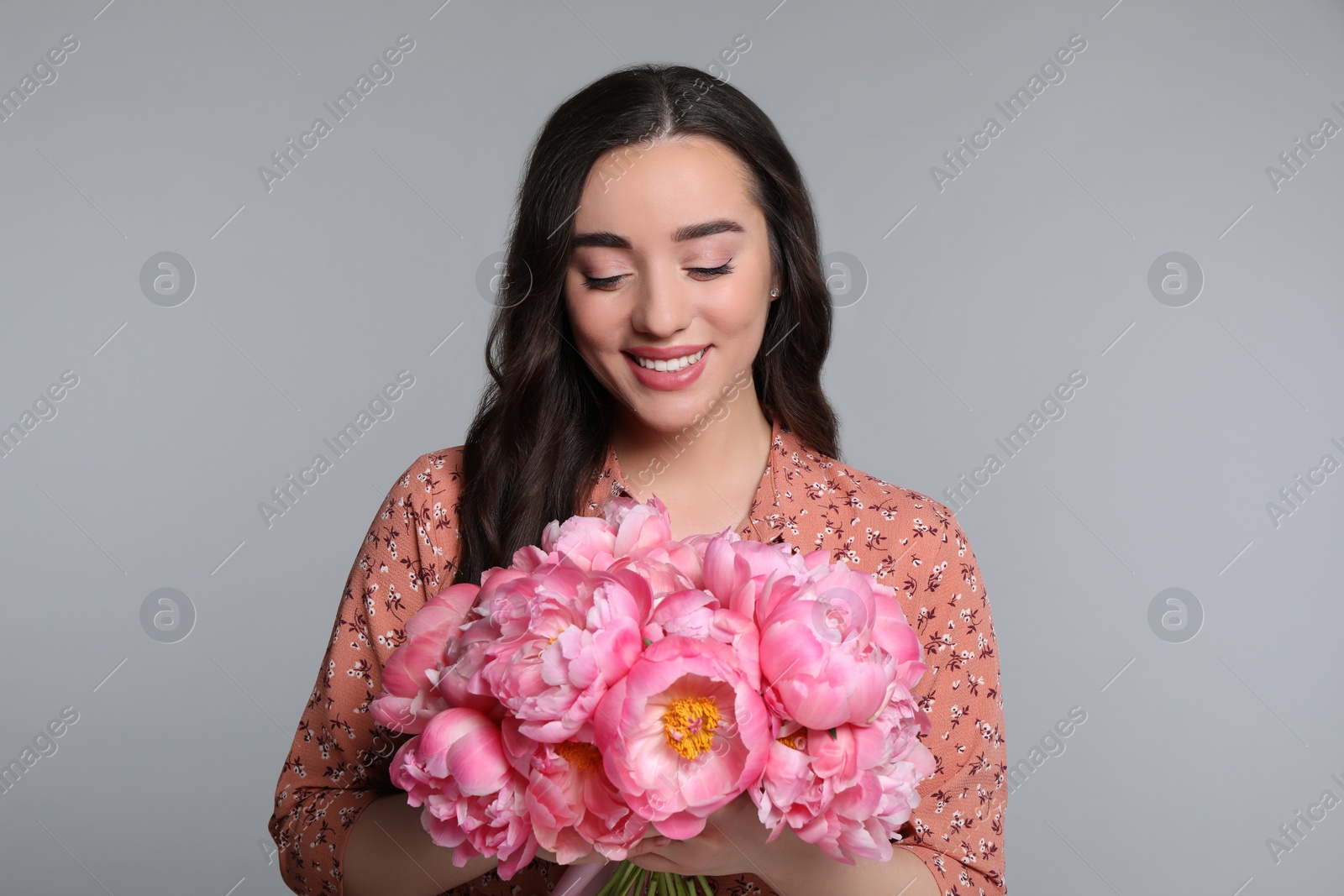 Photo of Beautiful young woman with bouquet of peonies on light grey background