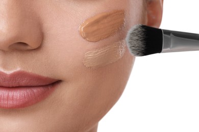 Woman applying foundation on face with brush against white background, closeup