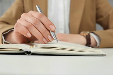 Woman writing in notebook at white table, closeup