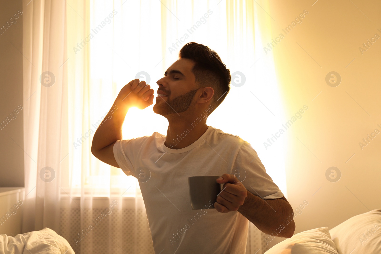 Photo of Young man with cup of coffee on bed at home. Lazy morning