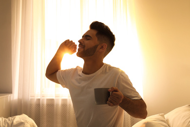 Photo of Young man with cup of coffee on bed at home. Lazy morning