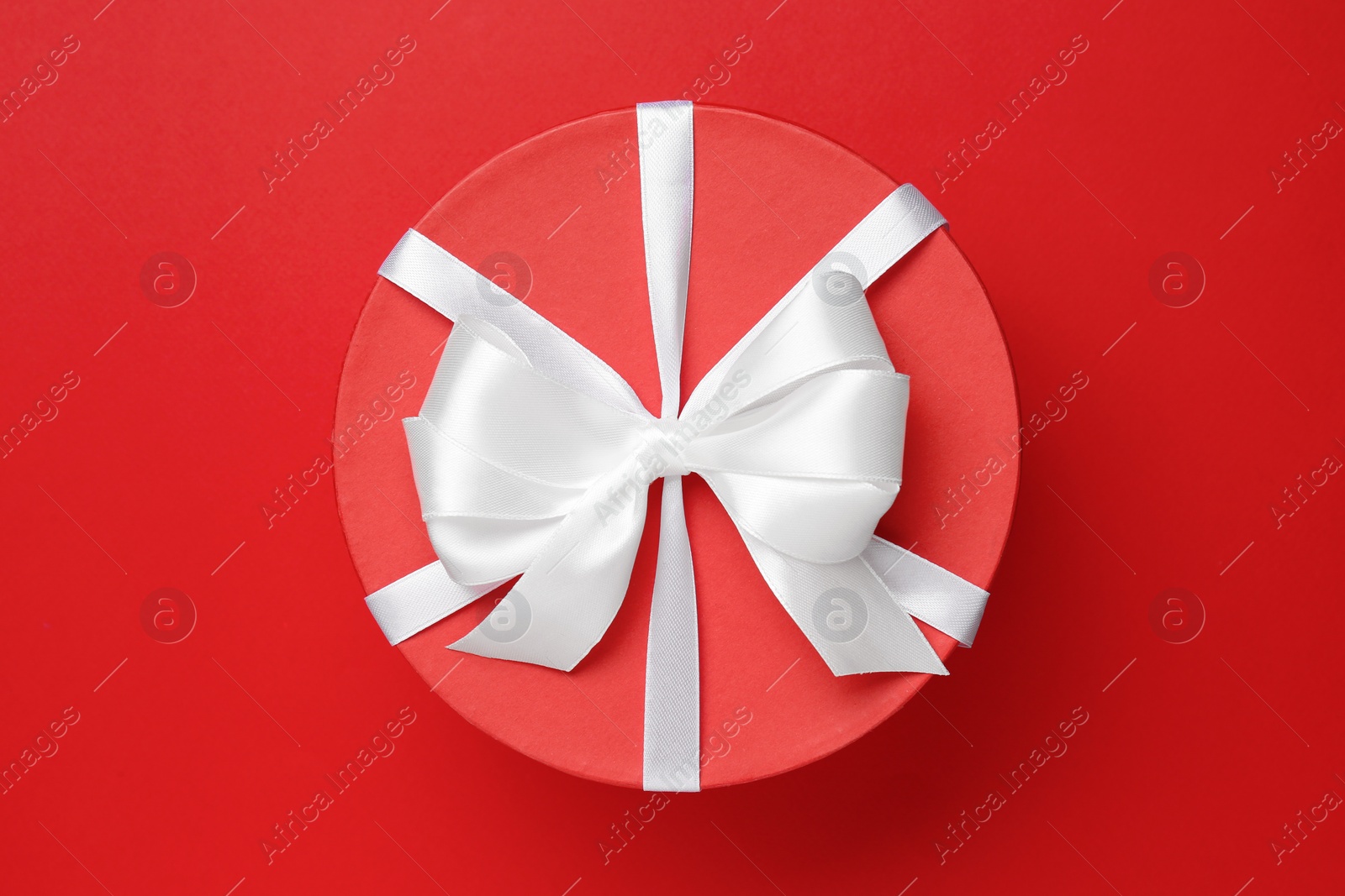 Photo of Beautiful gift box with white bow on red background, top view