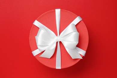 Photo of Beautiful gift box with white bow on red background, top view