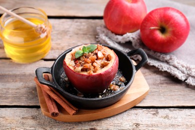 Photo of Tasty baked apple with nuts, honey and mint in baking dish on wooden table