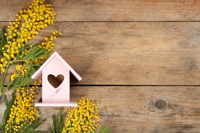 Stylish bird house and fresh mimosas on wooden background, flat lay. Space for text