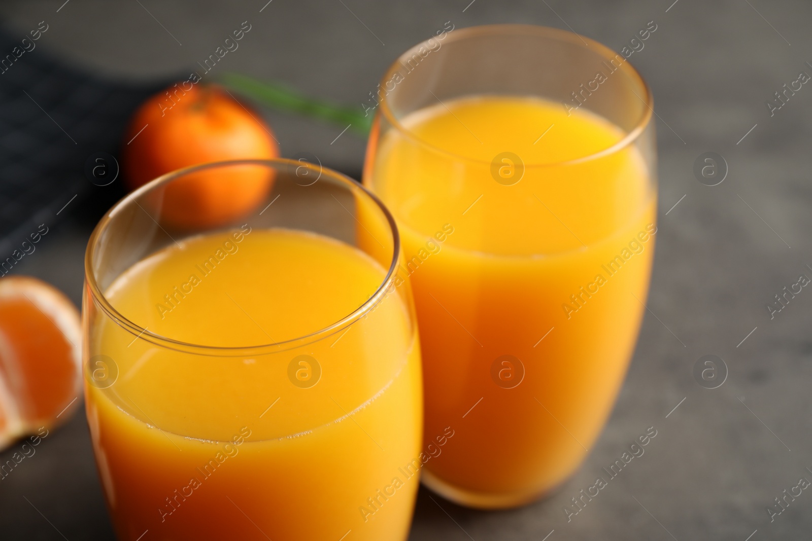 Photo of Glasses of fresh tangerine juice on grey table, closeup