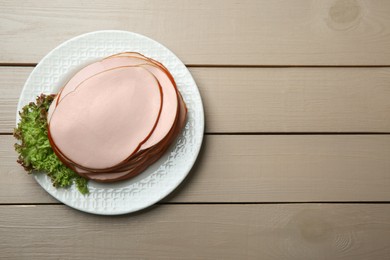 Photo of Slices of delicious boiled sausage with lettuce on beige wooden table, top view. Space for text